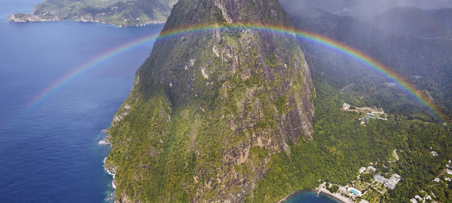 A Rainbow Over A Body Of Water With Pitons In The Background