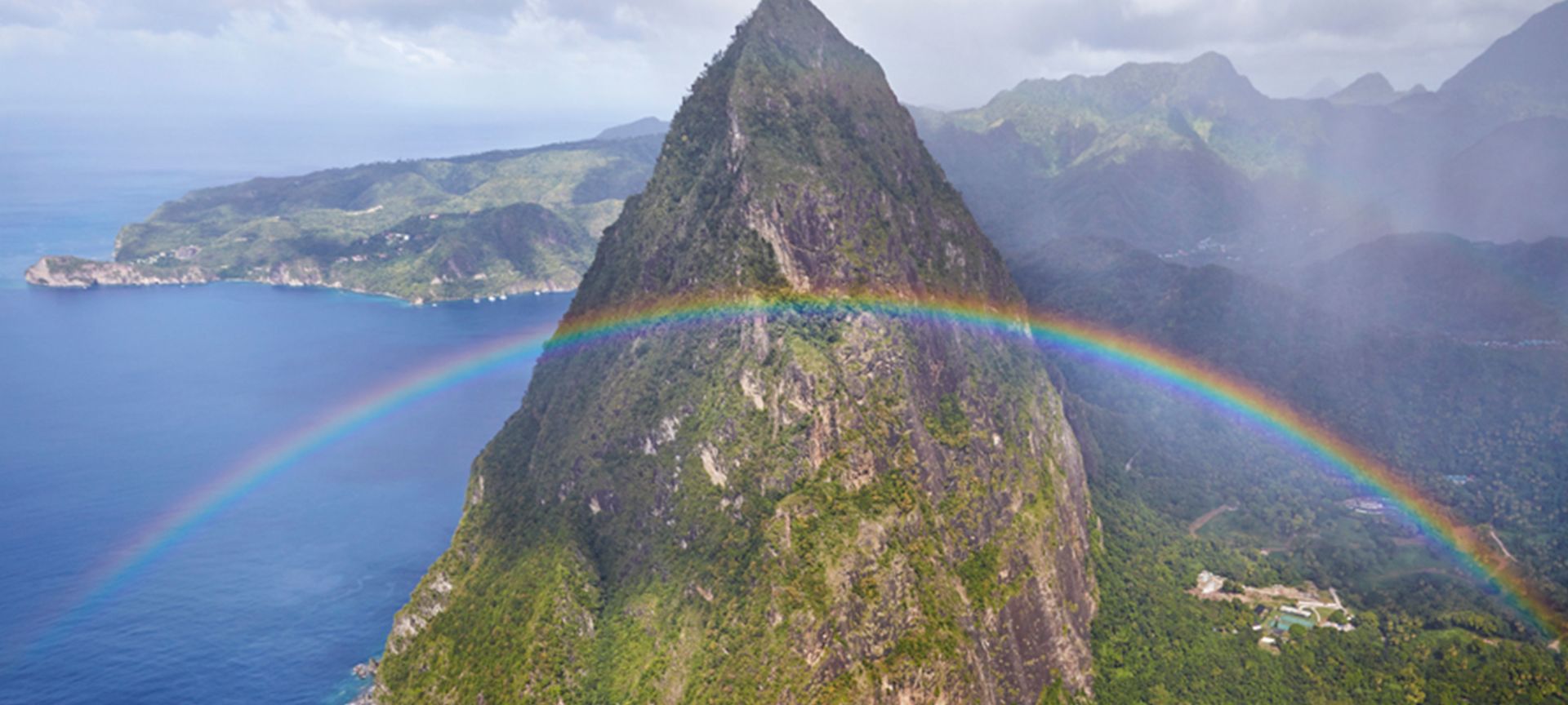 A Rainbow Over A Body Of Water With A Mountain In The Background