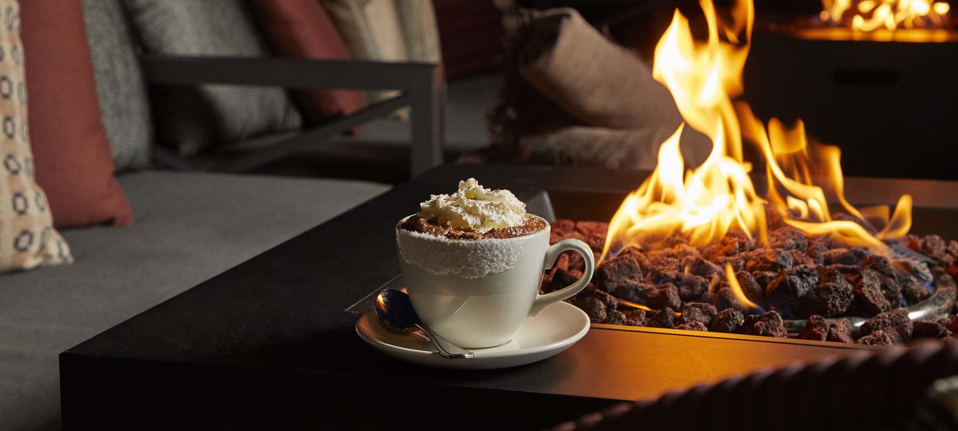 A Cup Of Coffee Sitting Next To A Fireplace
