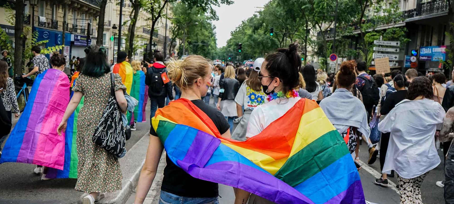 A Group Of People Walking Down A Street Holding Rainbow Flag