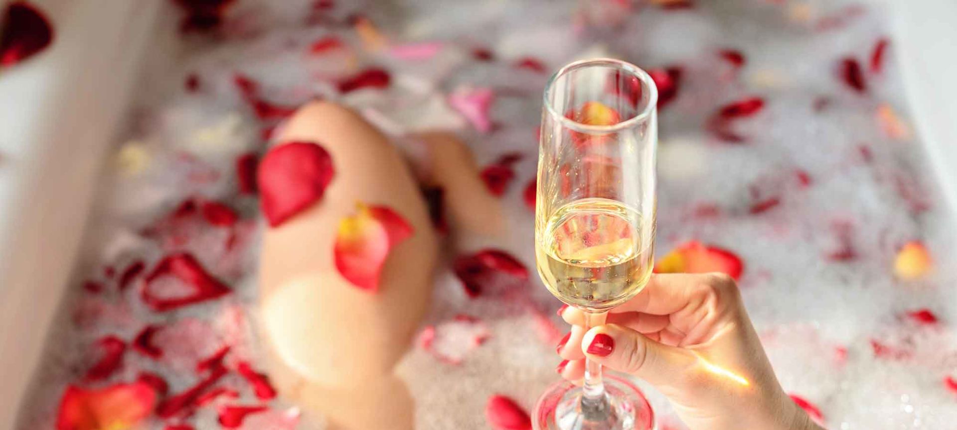 A Bathtub with Rose Petals and Hand Holding a Glass of Champagne